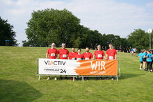 VIACTIV Firmenlauf 2024: fps Team steht in lauf-Outfits hinter Banner auf einer Wiese